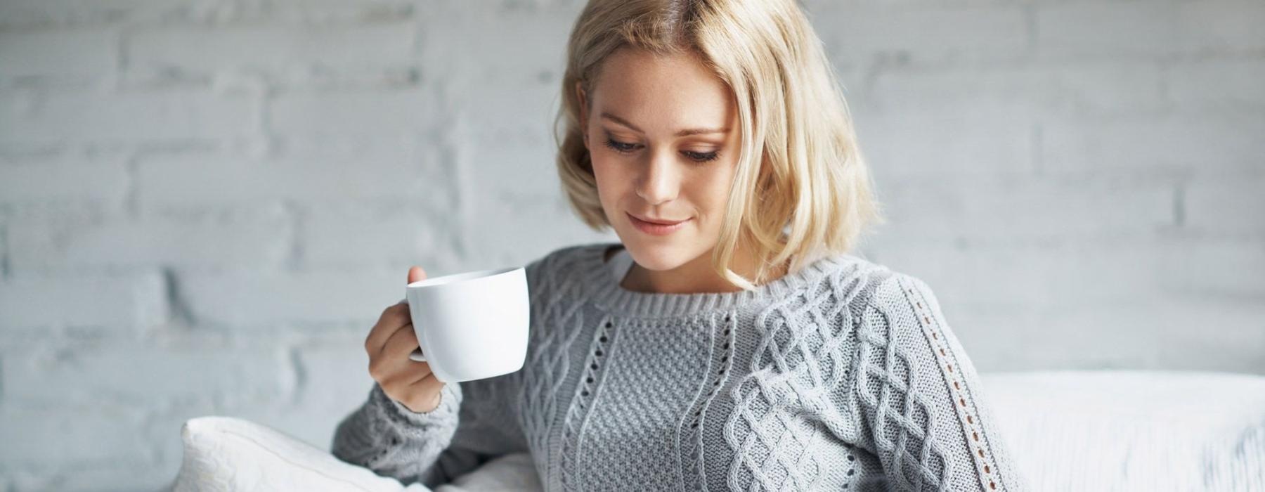 a woman sits on a couch with a cup of coffee and looks at her tablet